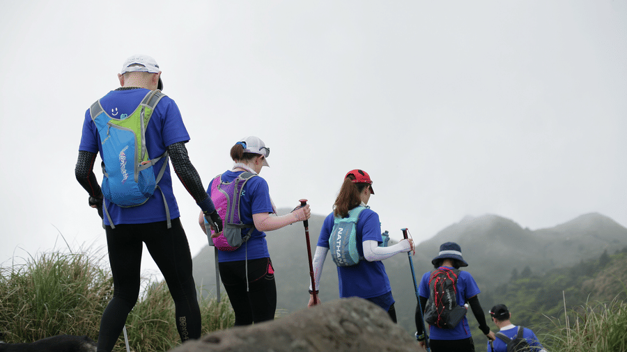 Group of hikers with backpacks walking on a rocky trail in a misty, mountainous landscape, suggesting an outdoor adventure