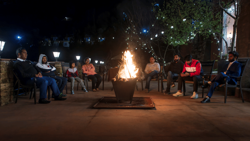  Under the night sky, a group of people are gathered around a warm, crackling bonfire, enjoying each other's company in an outdoor setting