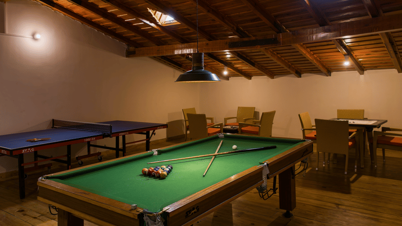 Inside a cosy recreation room with exposed wooden beams, a green billiard table and ping pong tables offer opportunities for indoor games