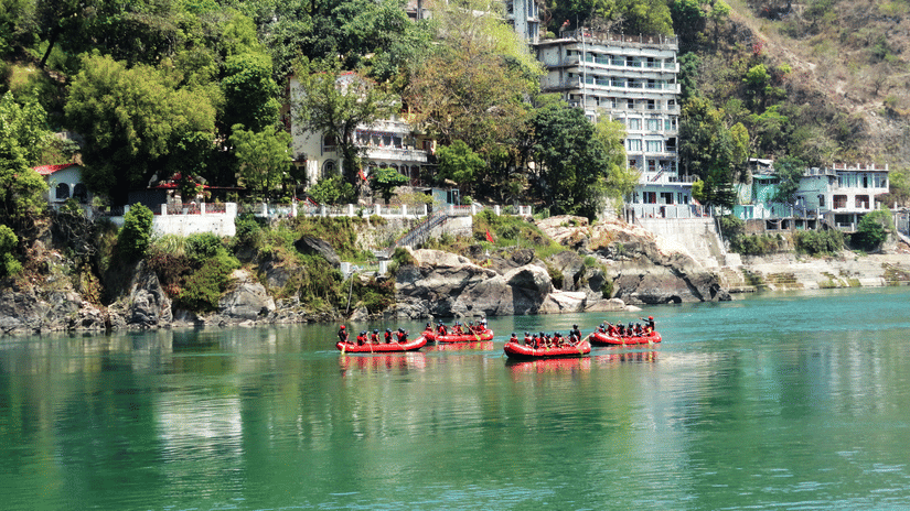 A scenic view of a tranquil river with red boats, flanked by lush green mountains and buildings