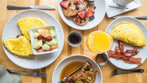 A vibrant breakfast spread on a wooden table with omelets, fruit, pancakes, and coffee