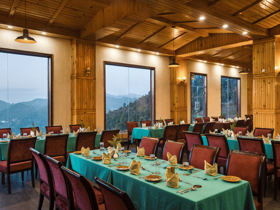  An elegant dining space with warm wooden interiors and expansive windows offering stunning valley views, creating a cozy and luxurious dining experience - Digantaa Resort in Mukteshwar