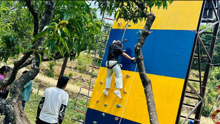 A vibrant climbing wall with colorful panels, attracting adventure seekers and families. People are visible nearby - Digantaa Resort in Mukteshwar