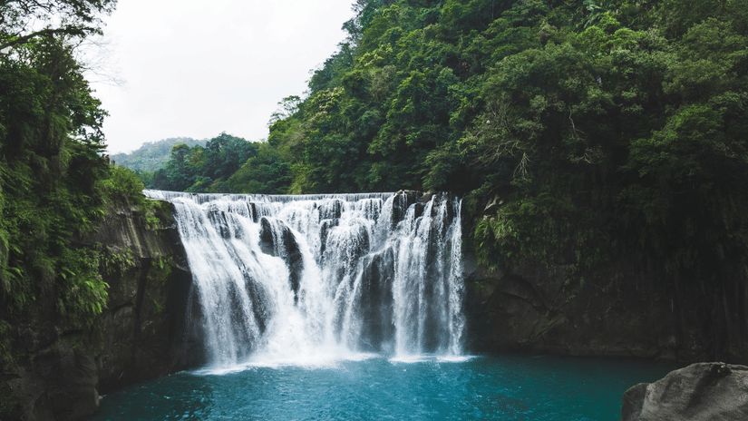 A majestic waterfall cascading into a turquoise pool, surrounded by lush green trees, creating a vibrant natural scene